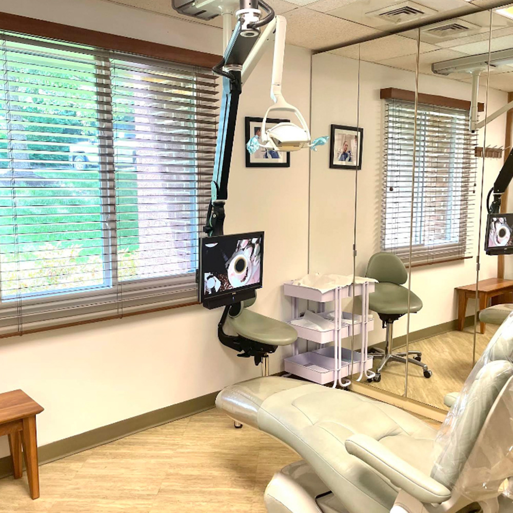 The image shows a dental office interior with a dental chair, a dental light, and various dental equipment.