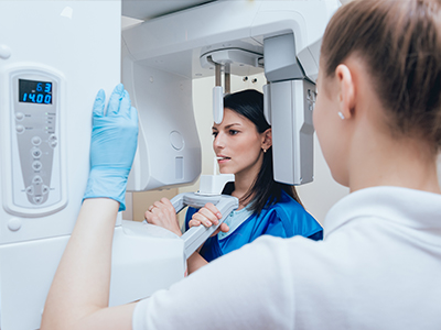 A woman in a blue lab coat is standing next to a large, modern 3D scanner with a digital display showing the word 'scan' and a timer reading '0:42,' while another person in a white lab coat is observing the scan.